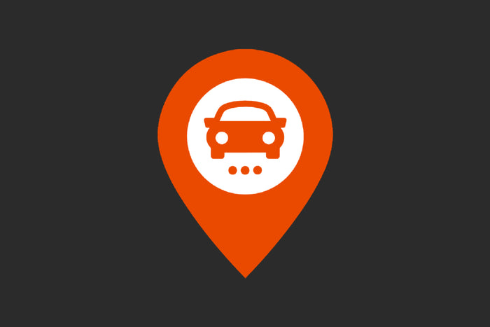 Orange map pin icon with a white circle in the center containing a orange car symbol and three dots underneath, indicating a vehicle location or car service point on a dark background.